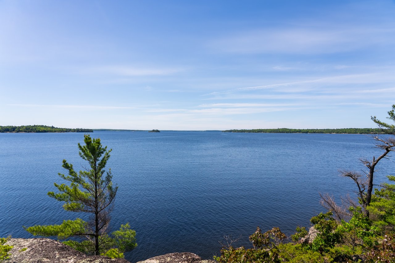 Calm lake view in the District of Parry Sound with pine and granite shoreline, representing Ontario cottage country.