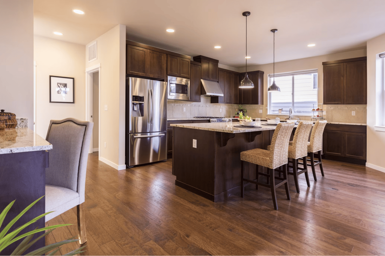 Kitchen with dark wood cabinetry, stainless steel appliances, and a granite island with woven bar stools.