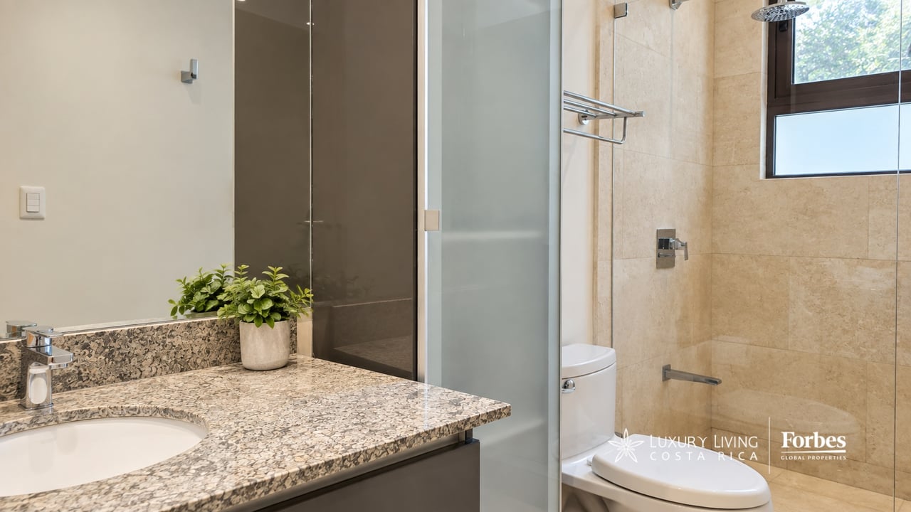 Modern bathroom with a speckled stone vanity, glass shower, beige tile, and a window.
