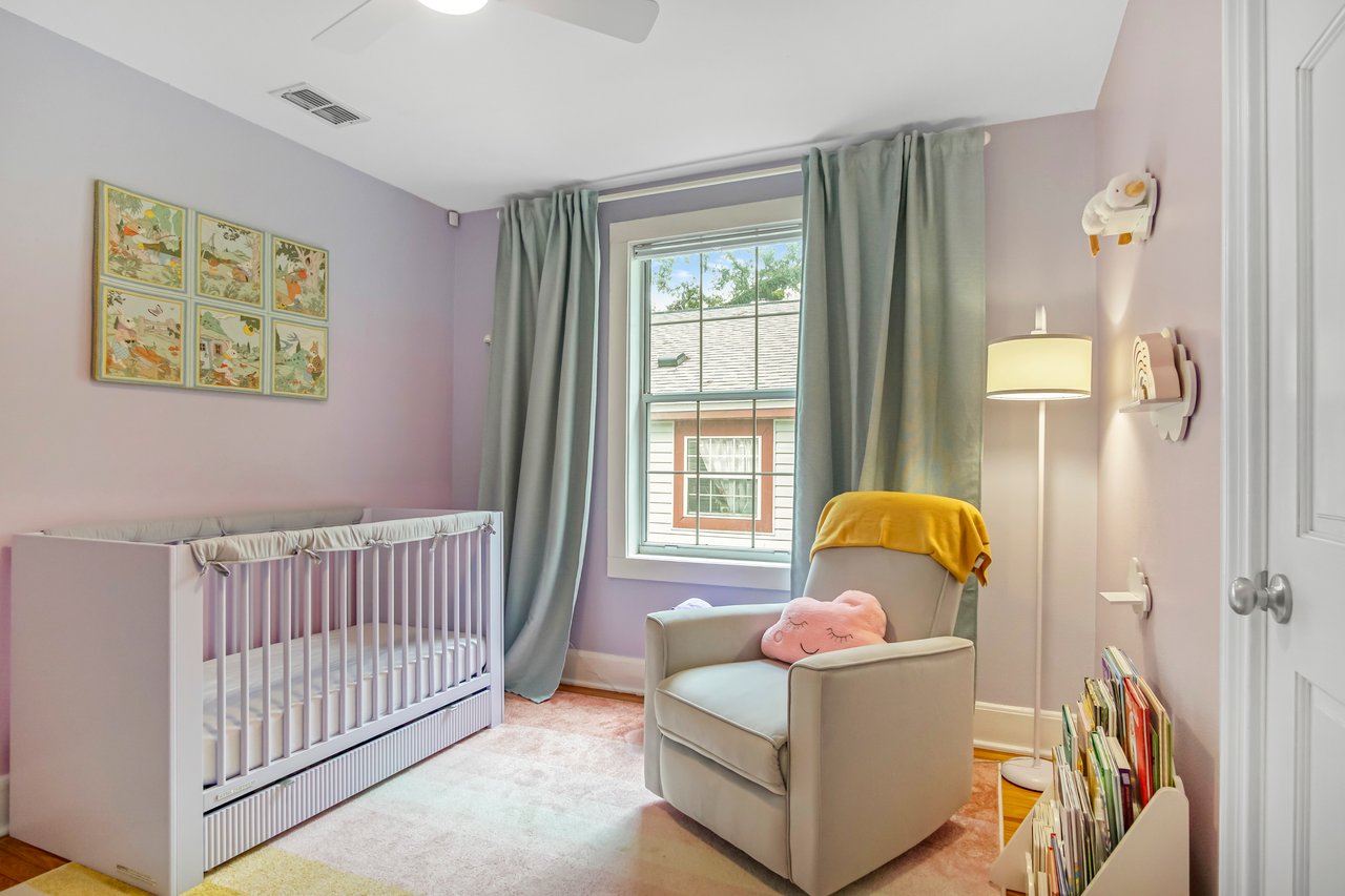 A cozy nursery with a lavender crib, plush chair with yellow blanket, soft pink walls, and a large window. Calm and inviting atmosphere.