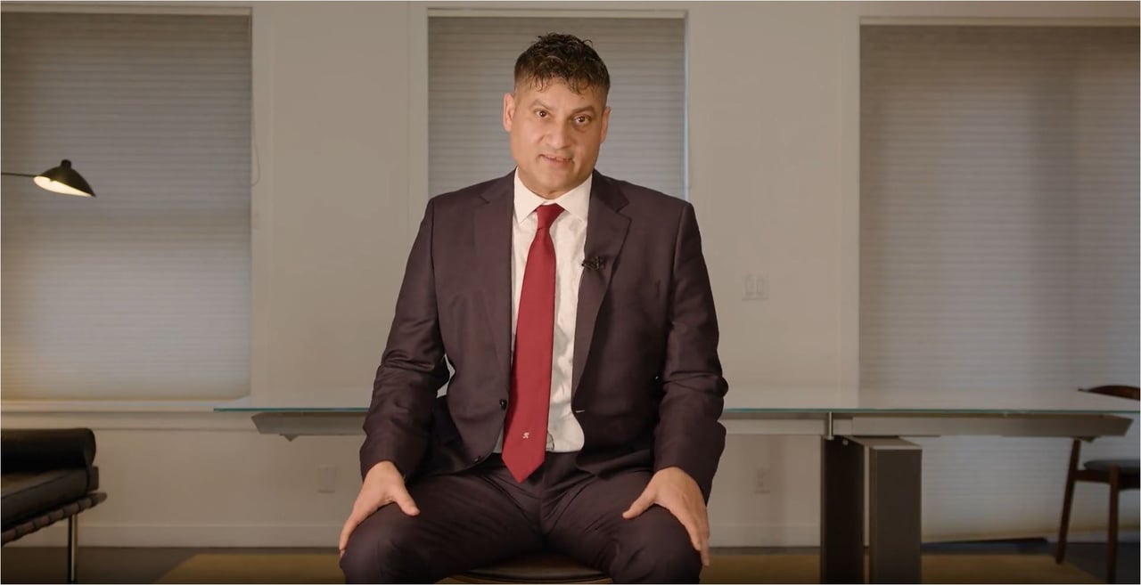 Reetesh Sood seated in a suit and red tie in an office.