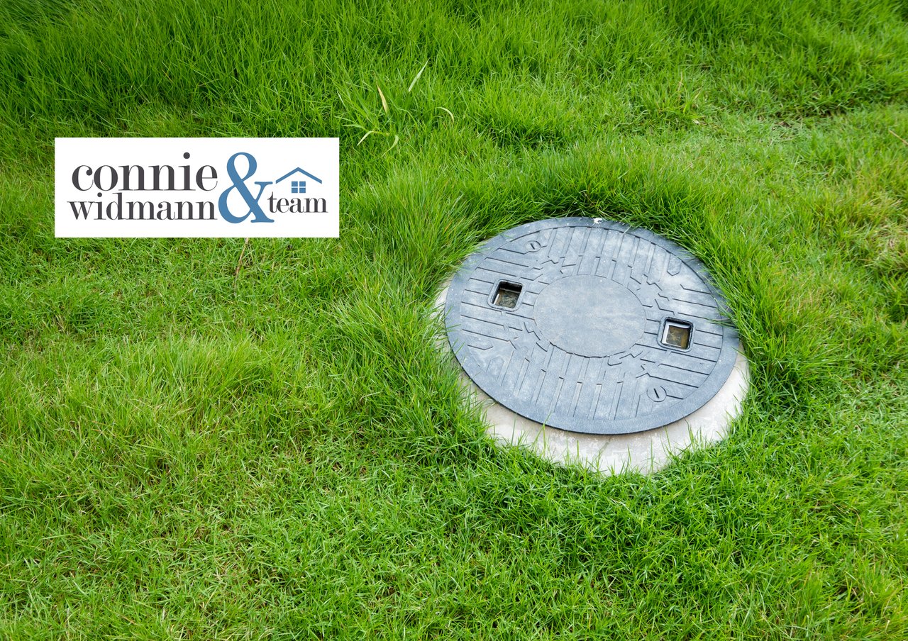 Round septic tank access cover set in grass, with the Connie & Widmann Team logo.