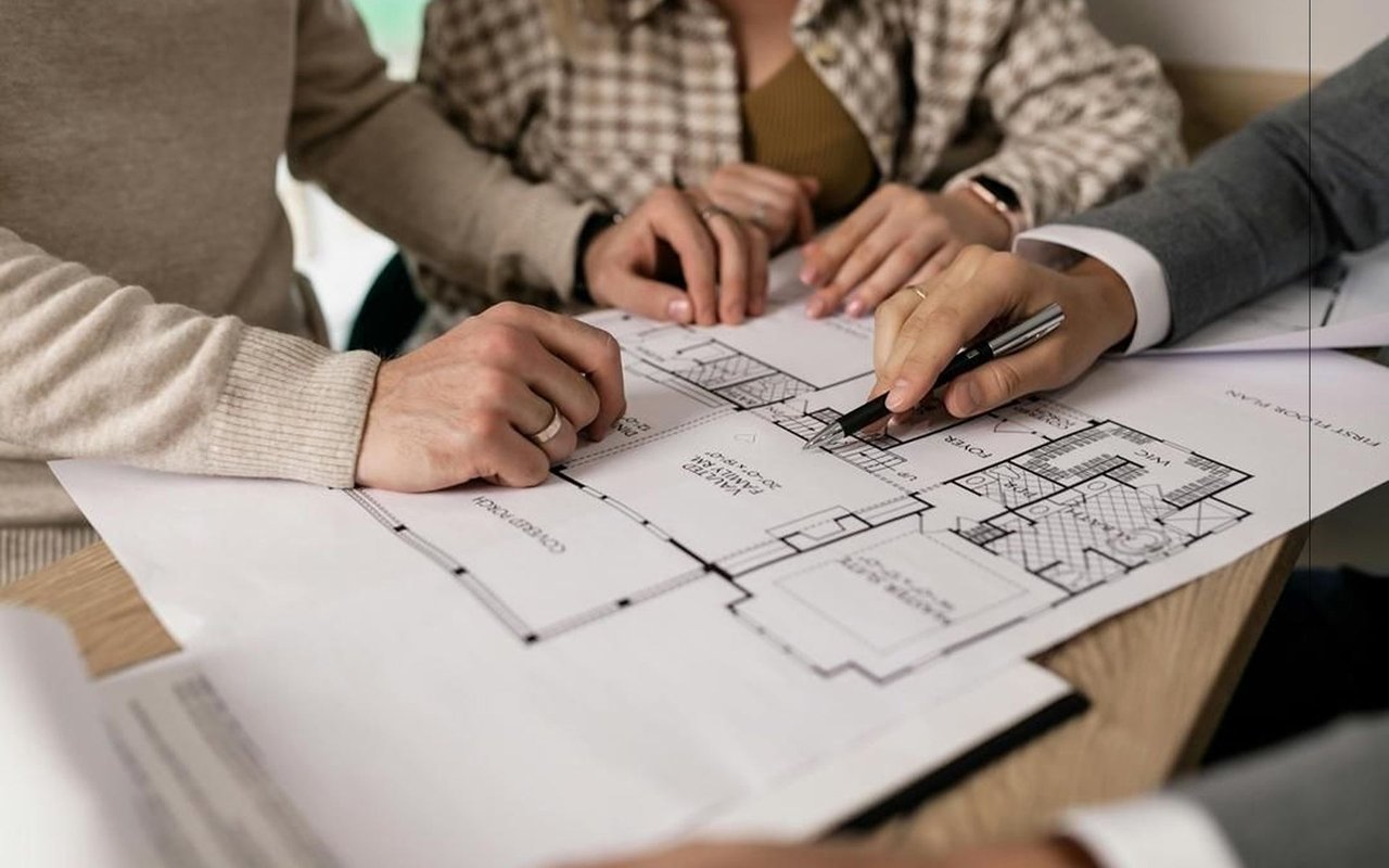 People review a home floor plan, with a pen pointing to the blueprint.