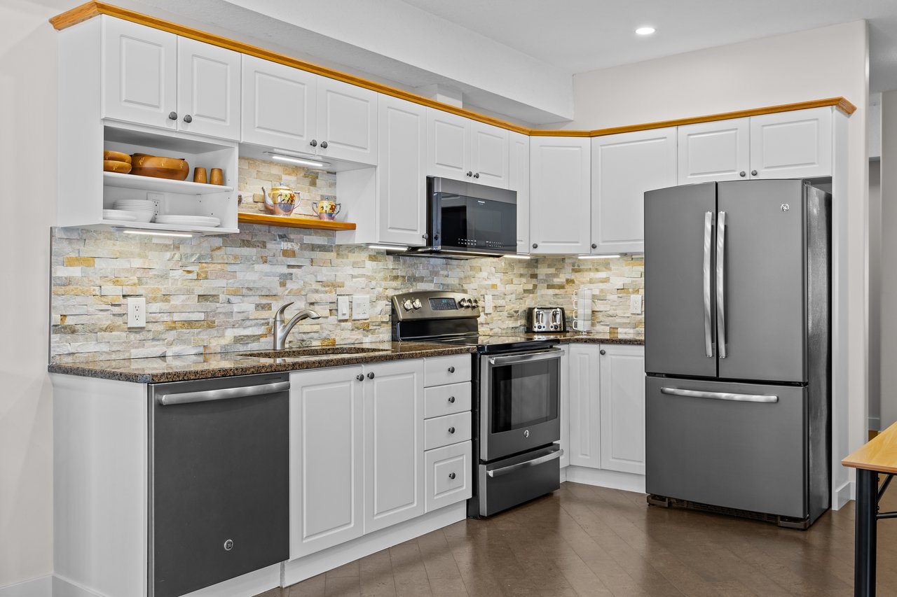 Kitchen with white cabinets, stone tile backsplash, granite counters, and stainless steel appliances.