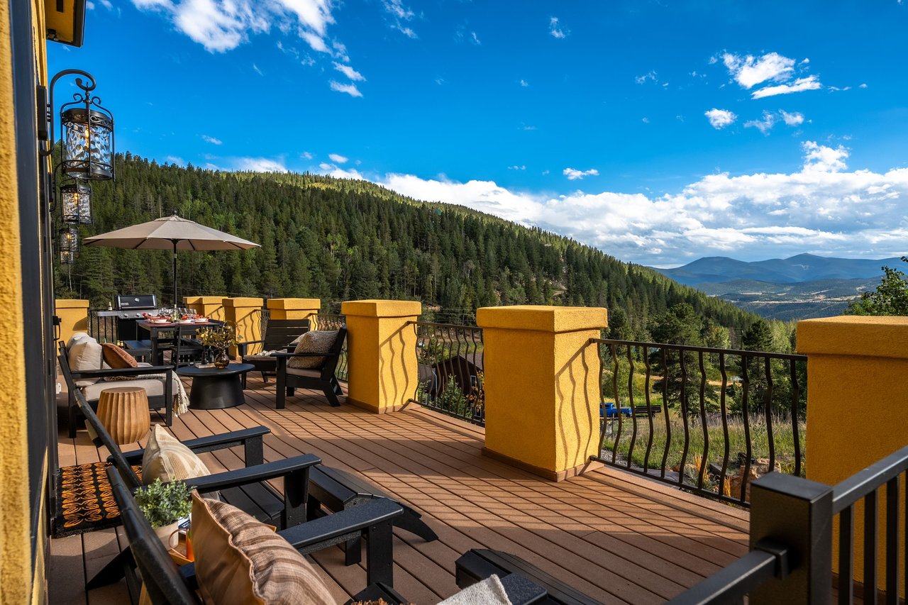 Furnished mountain-view deck with lounge seating, dining area, and yellow stucco pillars.