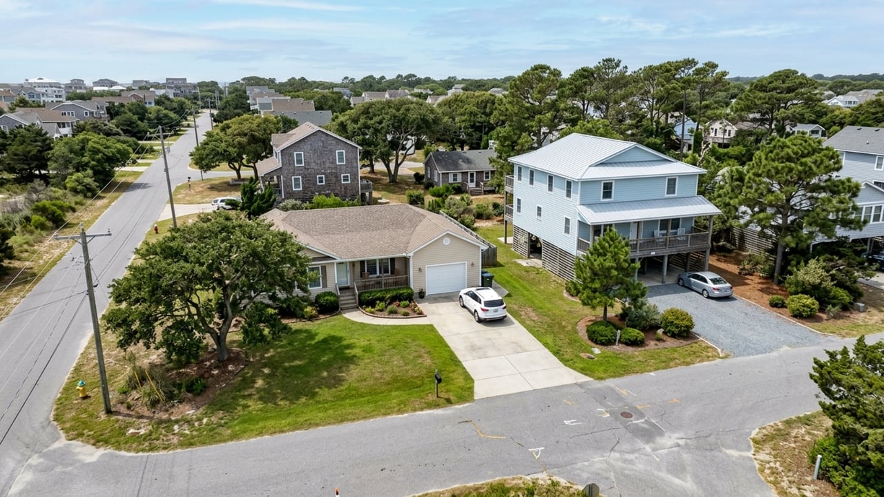 Aerial view of a leafy neighborhood with a raised pale blue house beside a beige home.
