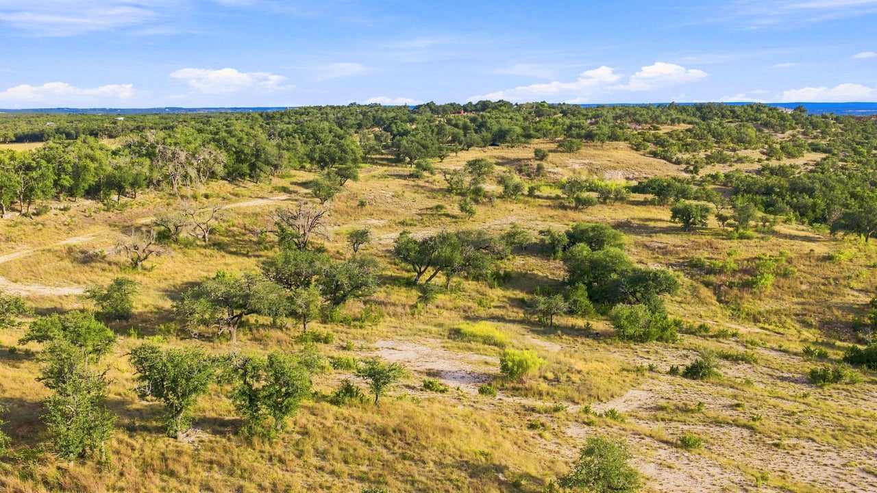 Aerial view of rolling ranchland with scattered oak trees, open grassland, and a dirt track.