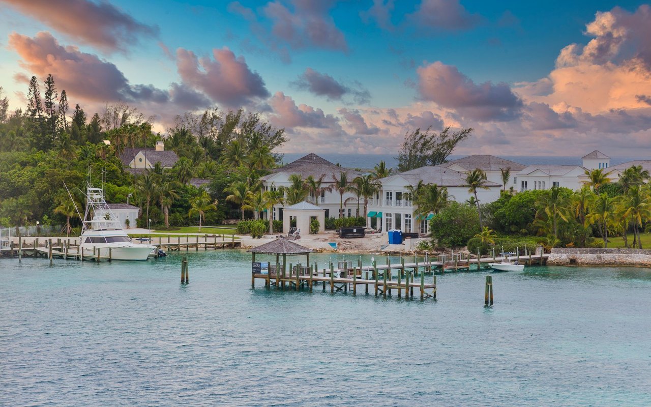 Lyford Cay waterfront homes and docks with a yacht on turquoise water at sunset.
