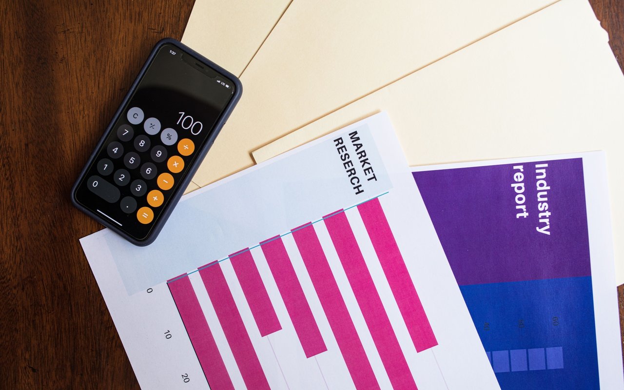 Calculator displaying 100 beside market research reports with magenta and blue bar charts.