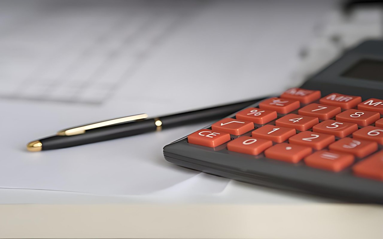 Calculator with orange keys and a black-and-gold pen resting on paperwork.