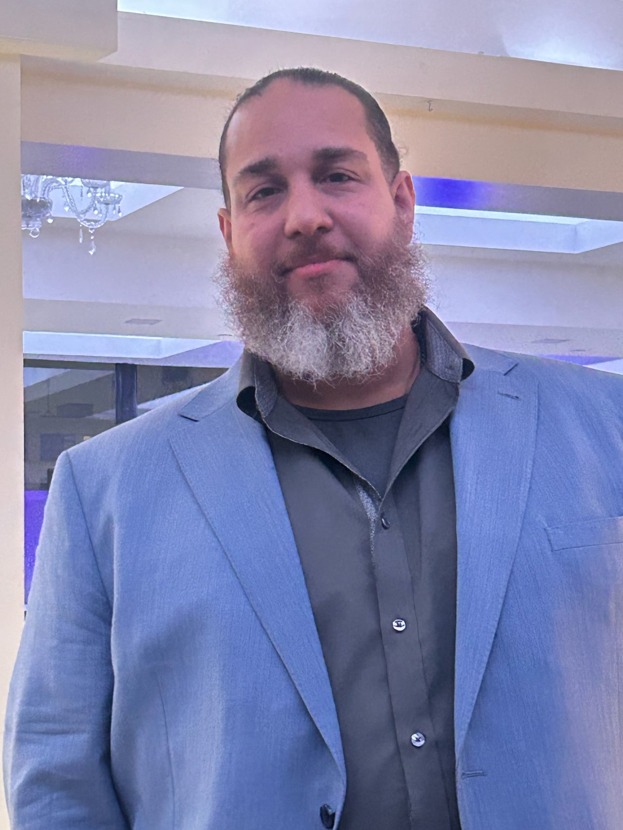 David Perez wearing a light blue blazer and dark shirt, with a long gray beard.