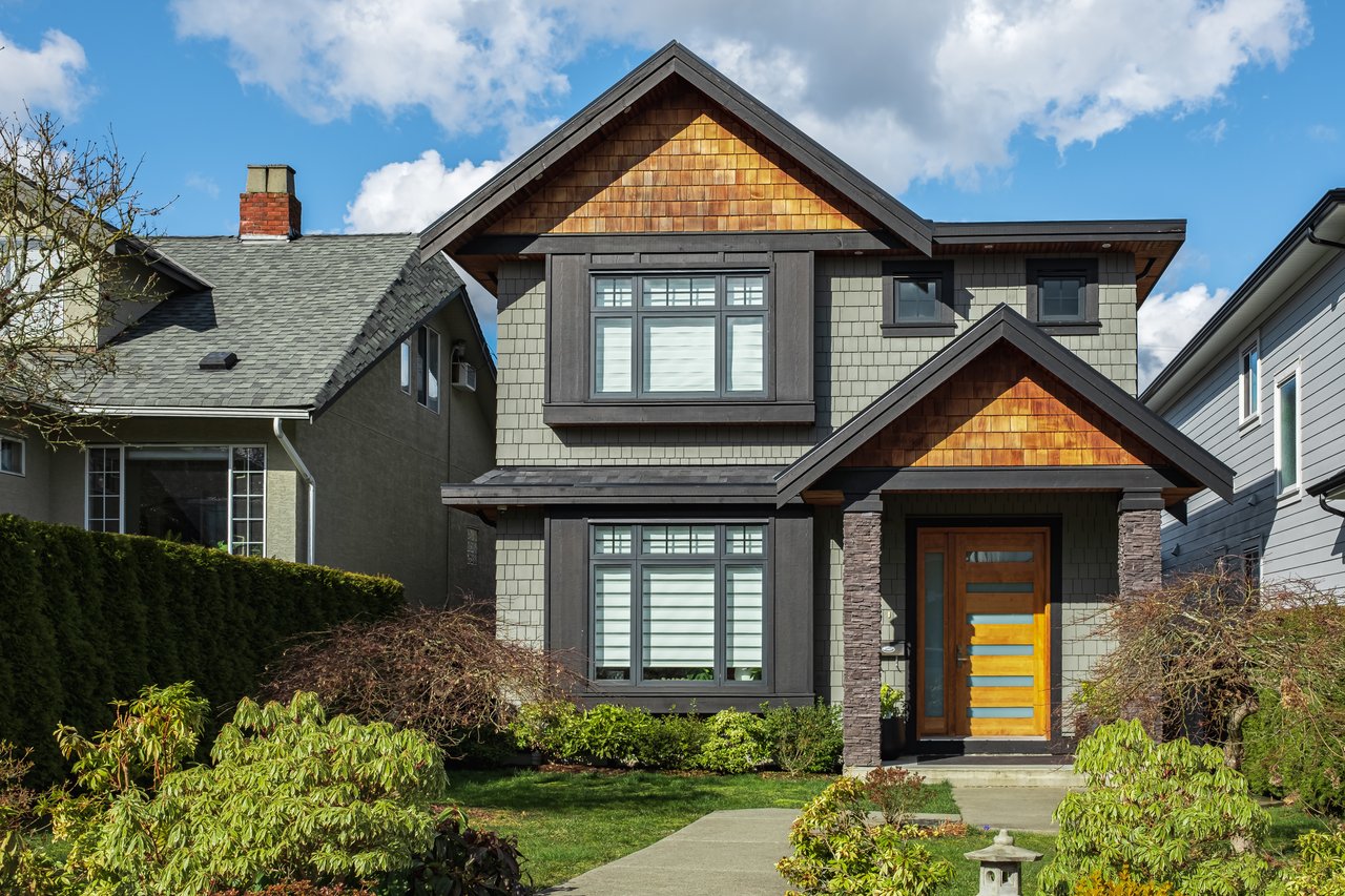 Two-story craftsman home with cedar-shingle gables, stone porch columns, and a colorful wood front door.