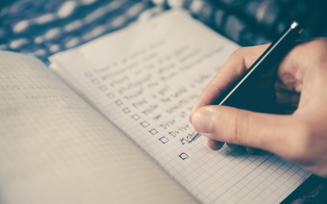 A hand writes on a graph-paper checklist with several marked boxes.
