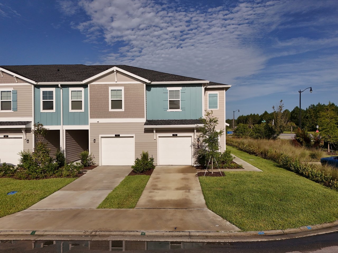Attached two-story townhomes with blue-green and beige siding, white garage doors, and landscaped driveways.