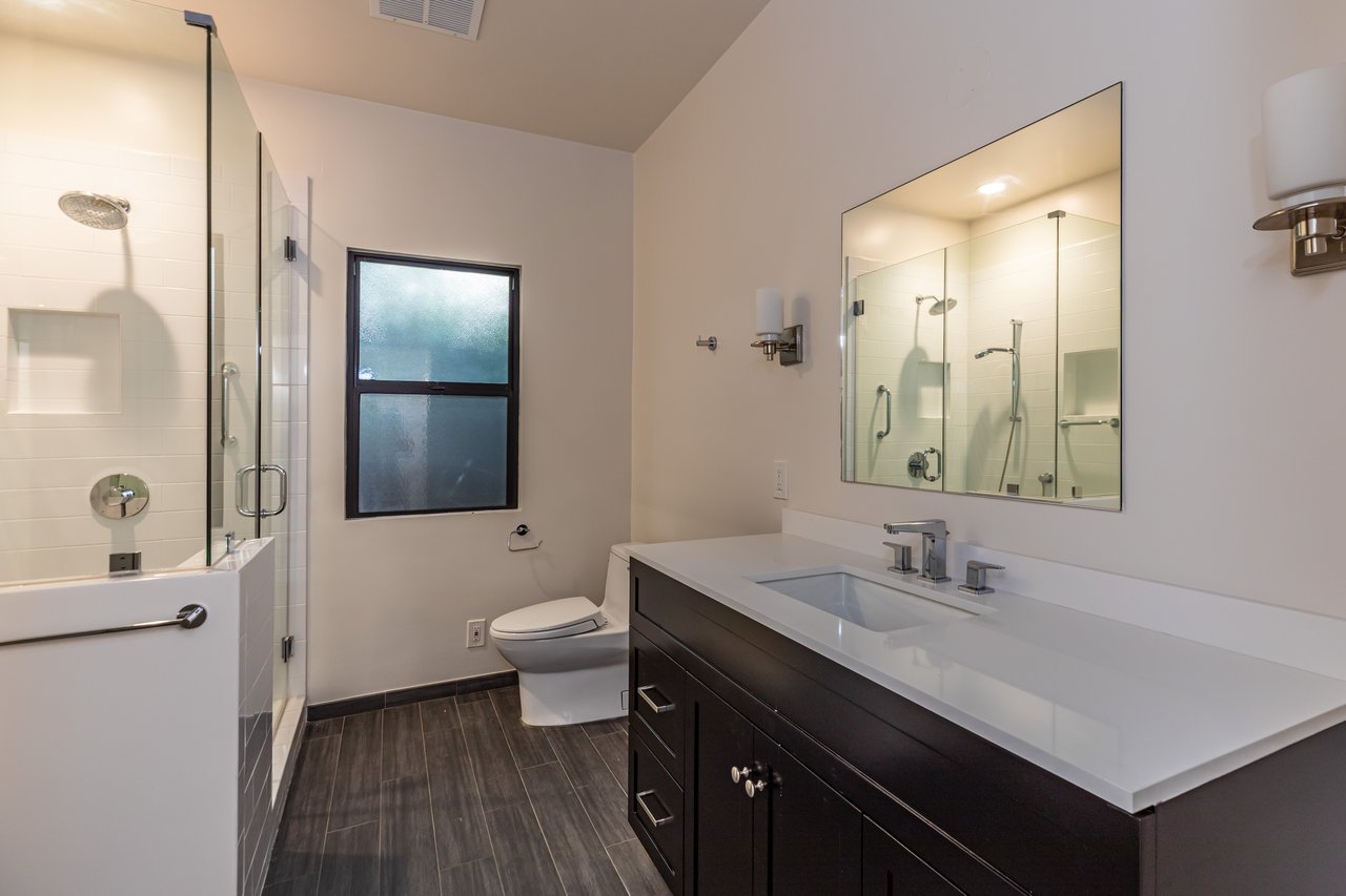 Modern bathroom with a glass shower, frosted window, and long dark-wood vanity.