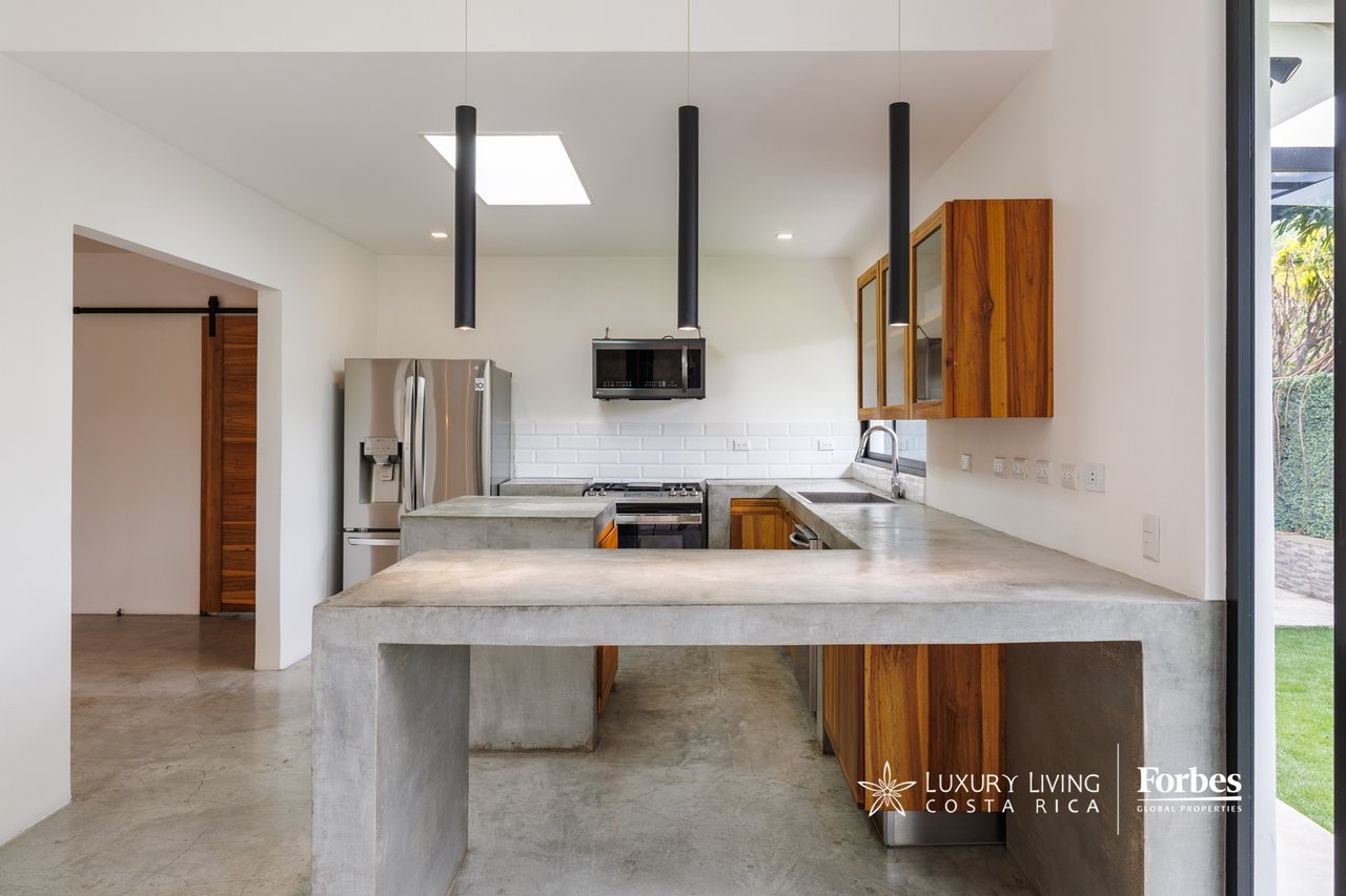 Modern kitchen with a large concrete peninsula, wood cabinetry, and stainless steel appliances.