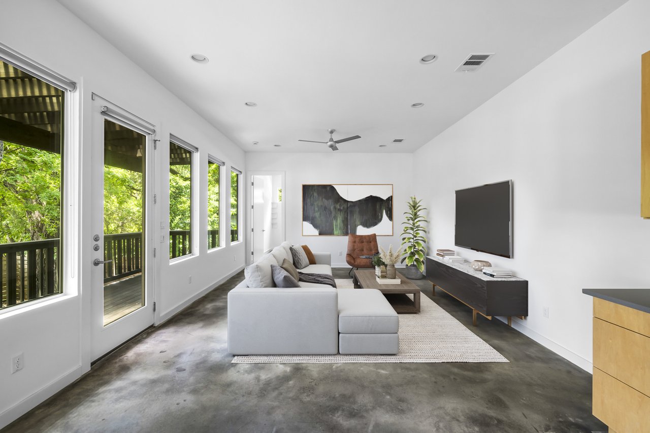 Second living room view at 1302 S 5th St Unit A, Bouldin, Austin, TX, with a wall-mounted TV, leather accent chair, and windows to the screened porch.