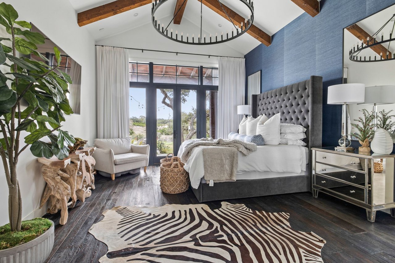 Primary bedroom with a blue accent wall, wood beams, and hardwood floors in this Creek Road Ranch home in Dripping Springs, Texas.