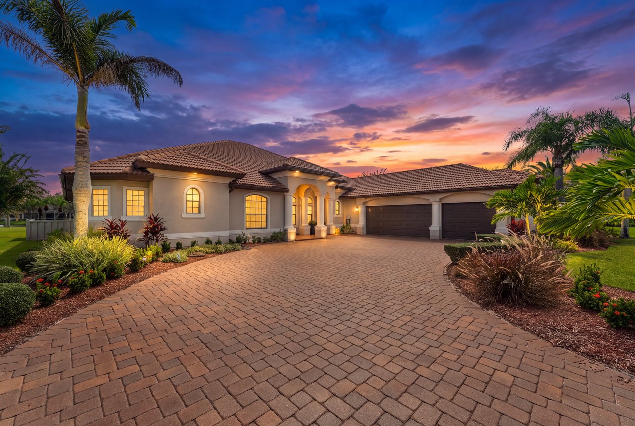 Stucco home with a tile roof, arched entry, and wide brick-paver driveway at sunset.