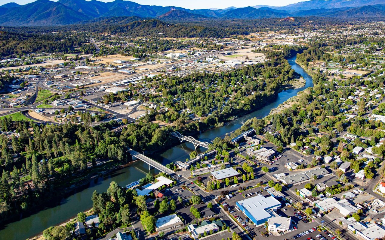 Aerial view of Tualatin with the river, bridges, neighborhoods, and forested mountains beyond.