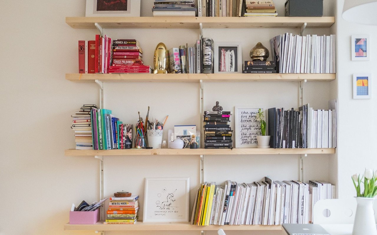 Wall shelves filled with books and artwork, with tulips and a laptop at the edge.