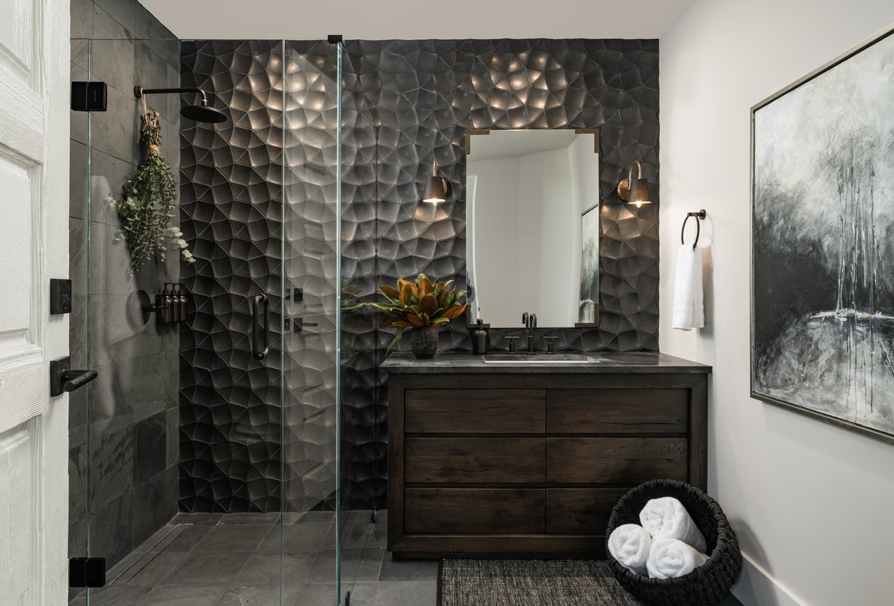 Modern bathroom with a glass shower, sculptural dark tile wall, and dark wood vanity.