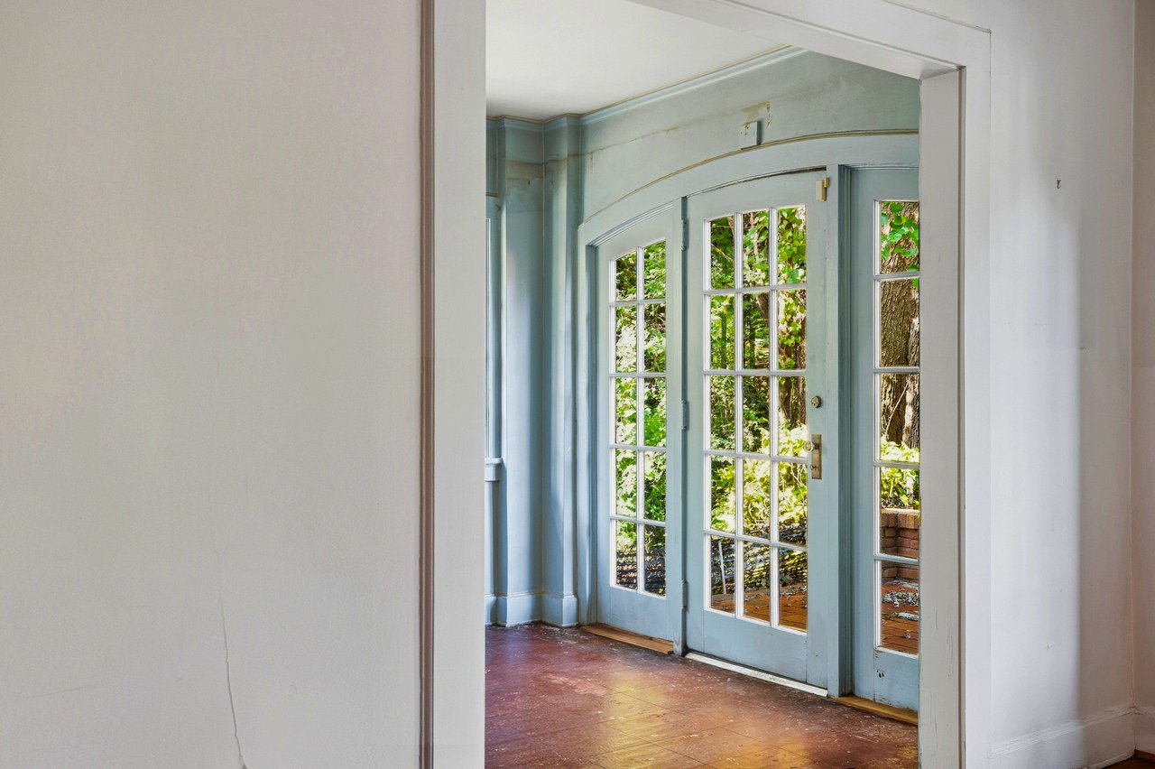 Empty room with pale blue French doors, sidelights, and a worn wood floor.