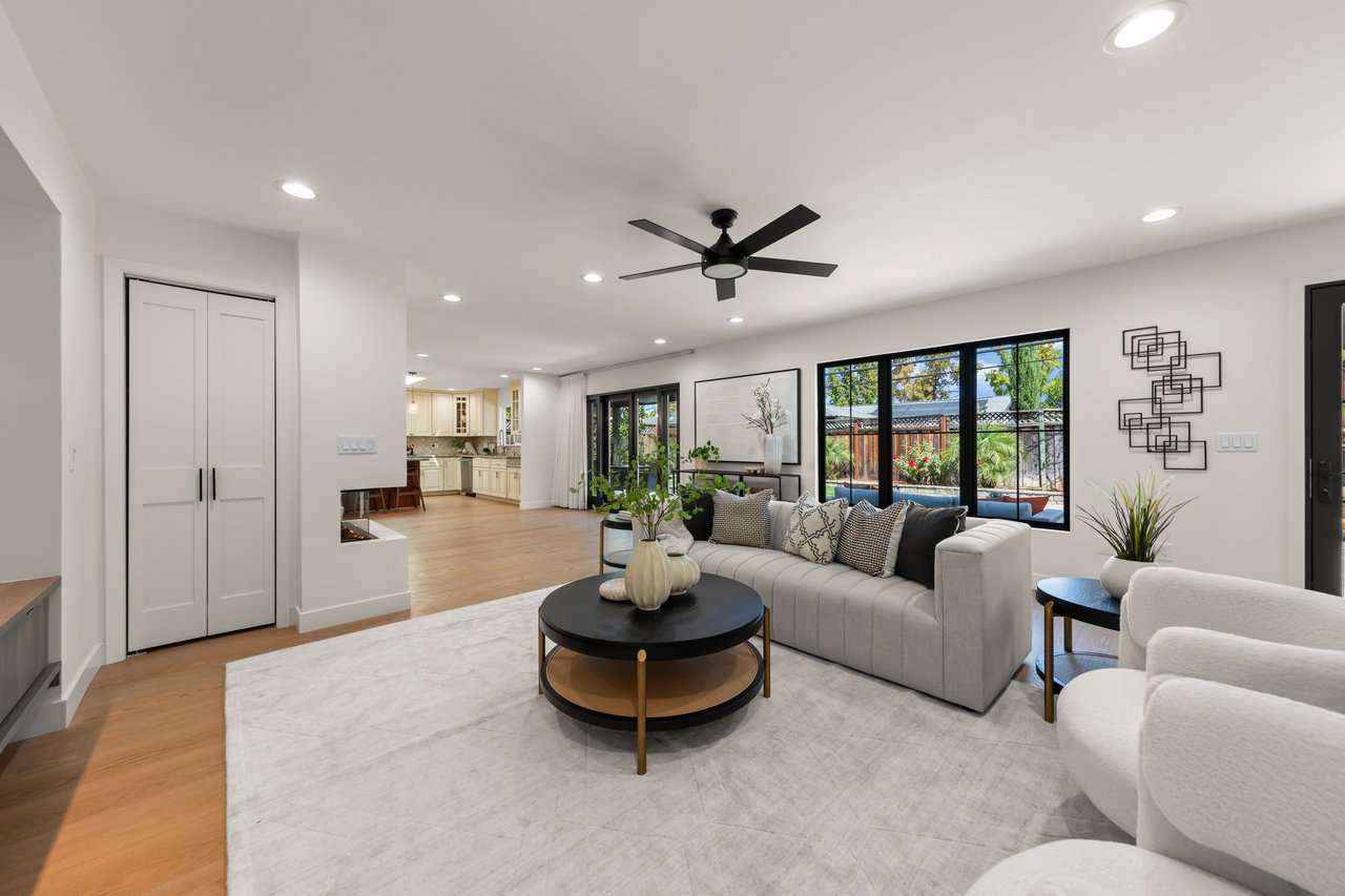 Staged living room with a pale sectional, black coffee table, and windows overlooking a backyard pool.