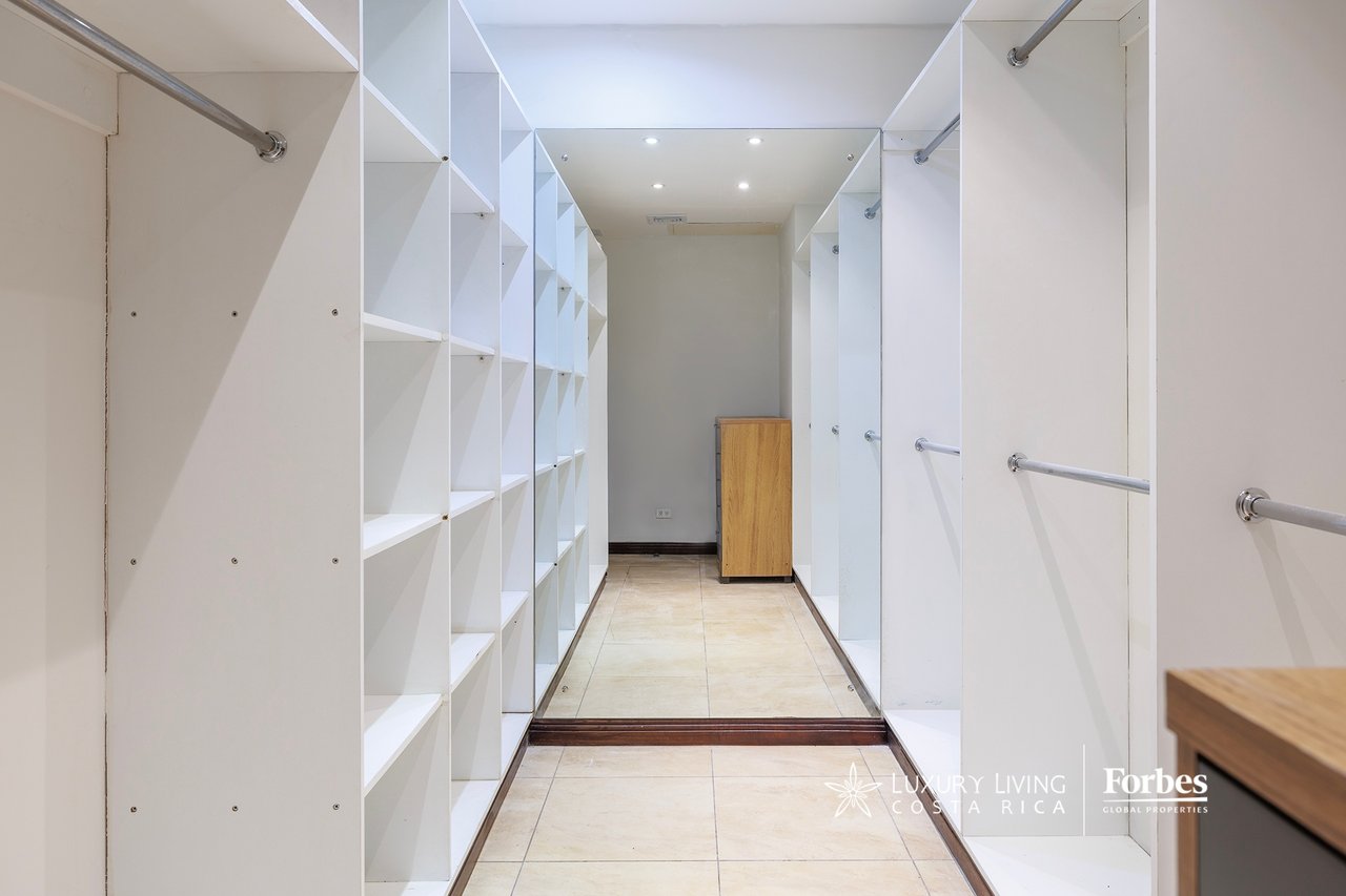 Walk-in closet with white built-in shelving, hanging rods, and a small wooden cabinet.