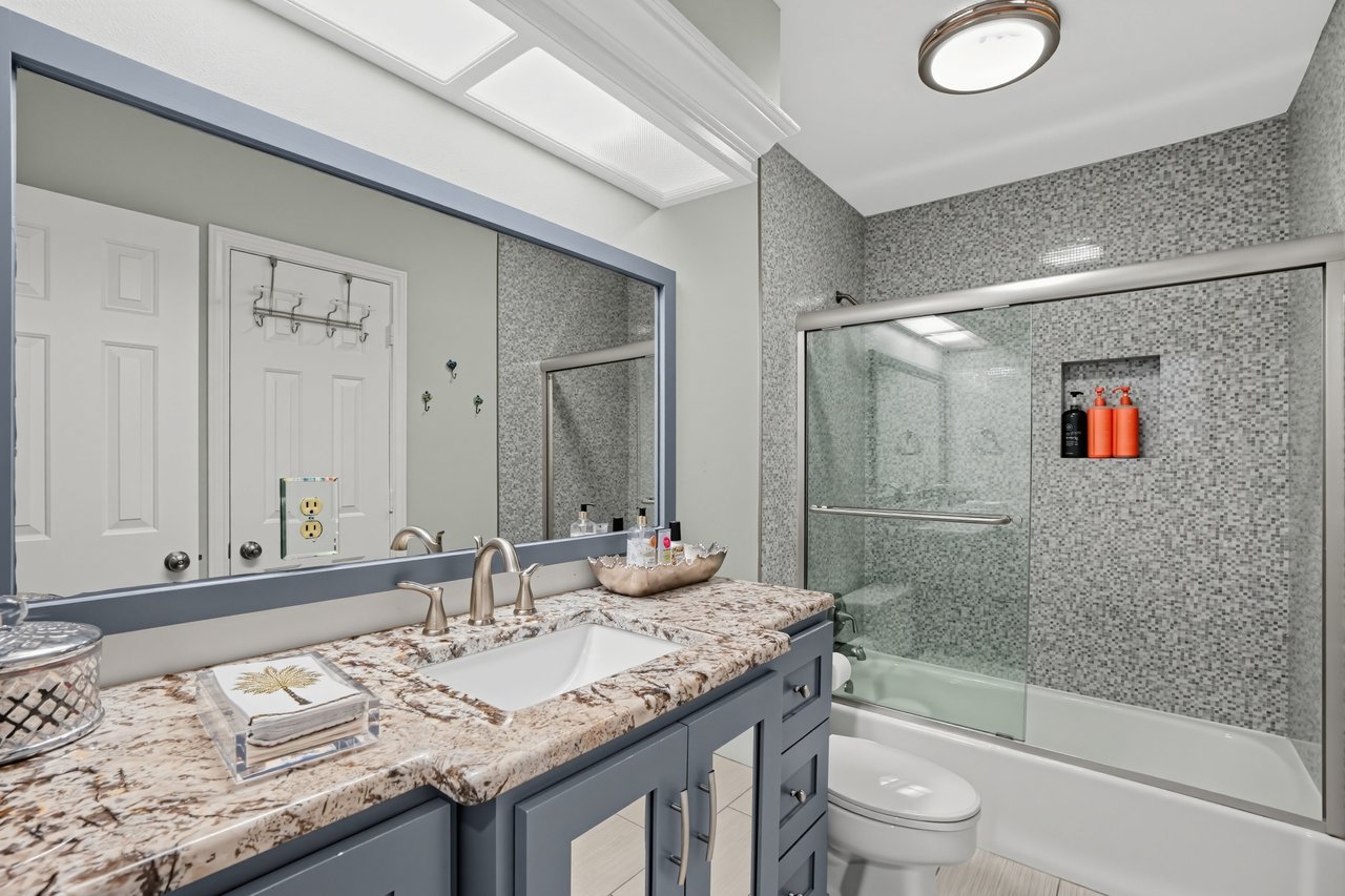 Bathroom with a gray vanity and granite counter beside a glass-enclosed tub and mosaic tile shower.