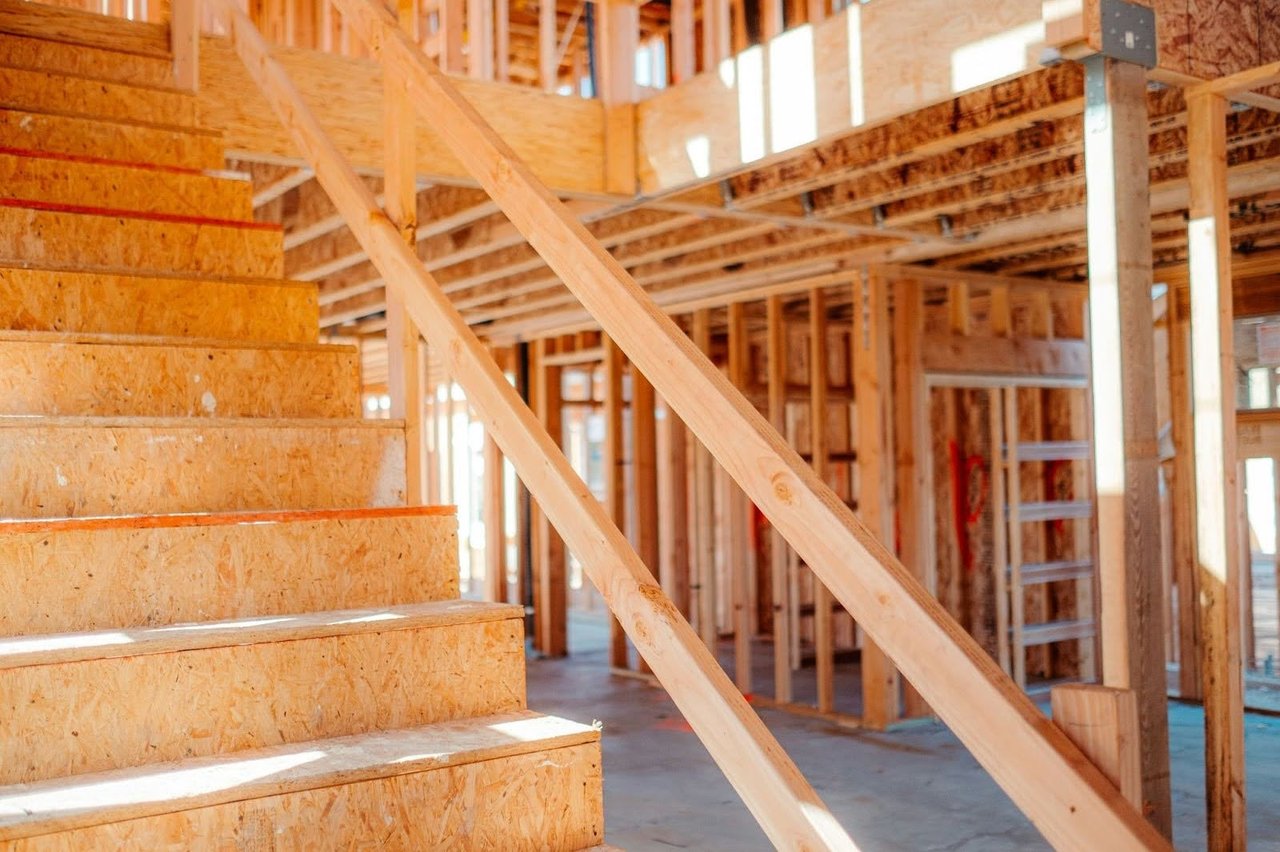 Custom luxury home construction site highlighting the rough-in framing phase, featuring wood studs, subfloor joists, and an OSB structural staircase.