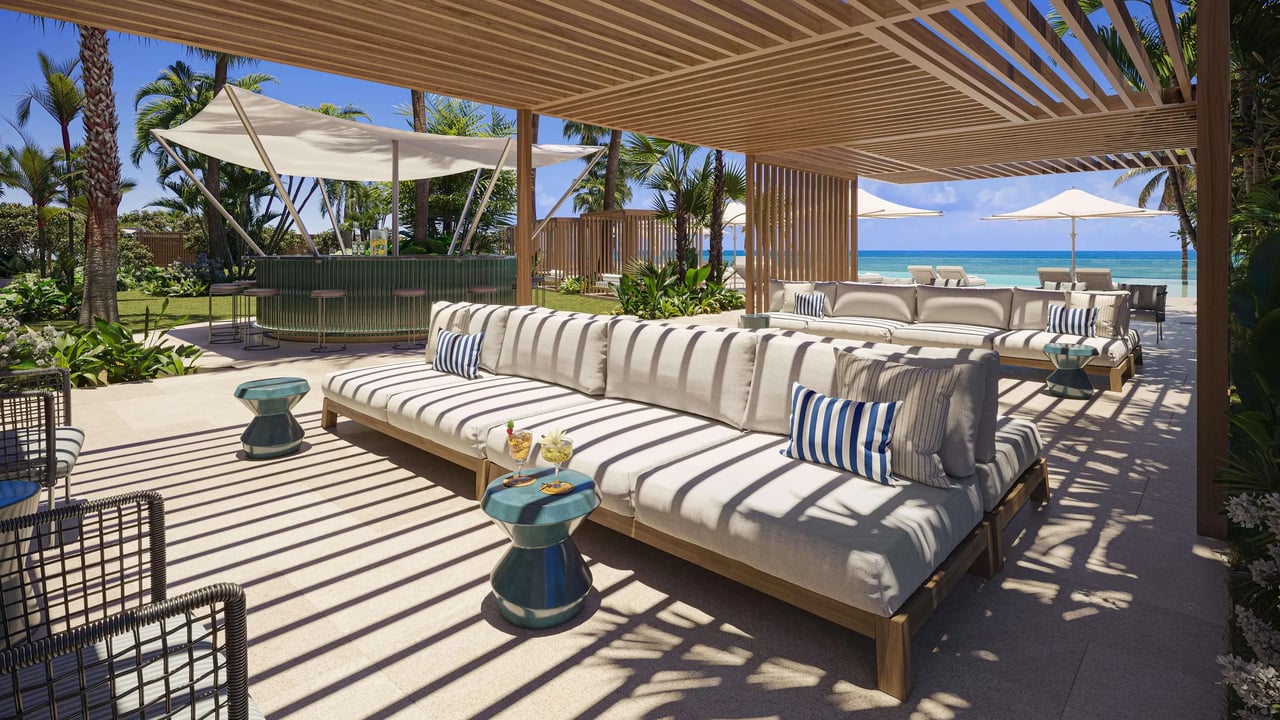 Furnished beachfront lounge beneath a timber pergola, with ocean views and striped cushions.