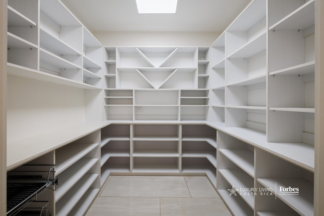 Walk-in pantry with white built-in shelving, wraparound counters, and a pull-out metal rack.