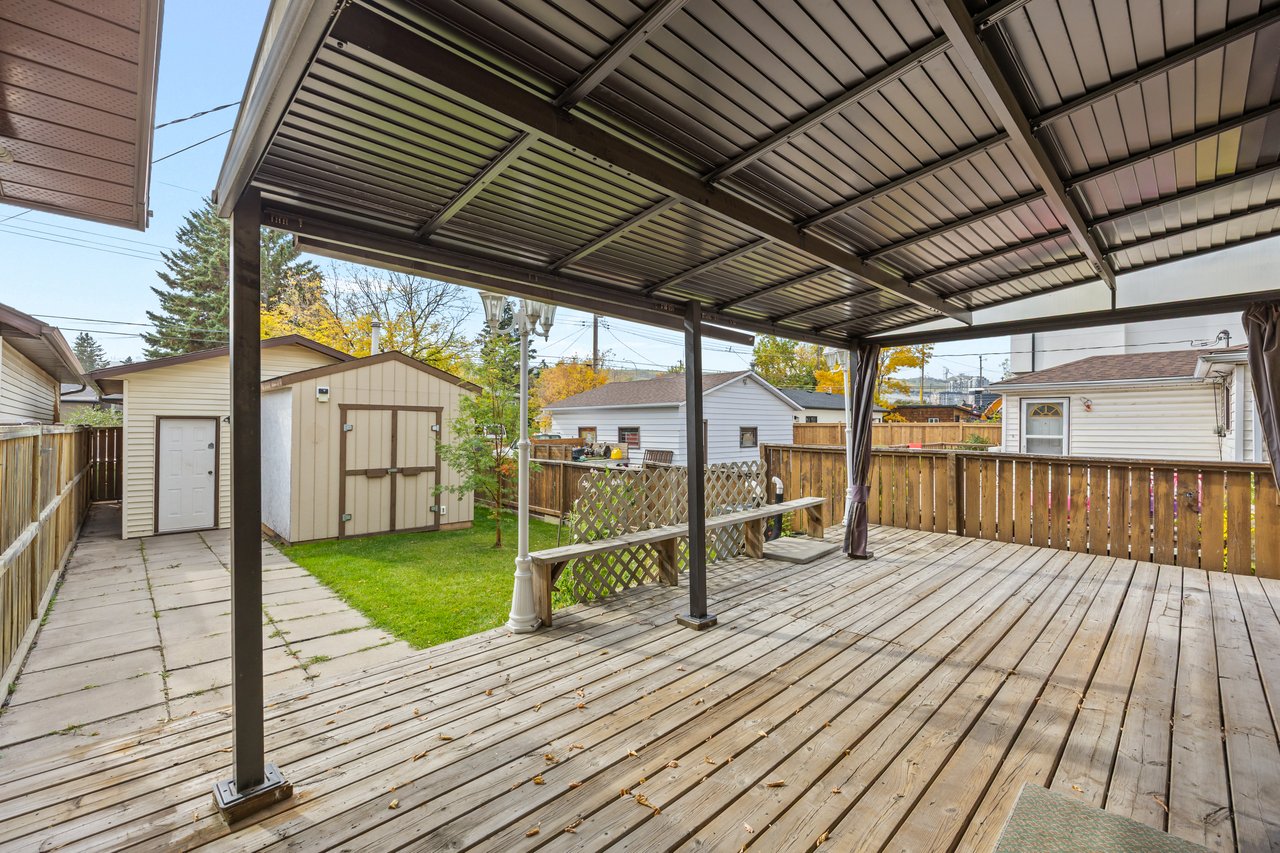 Covered backyard deck with a metal canopy, built-in bench, fenced lawn, and storage shed.