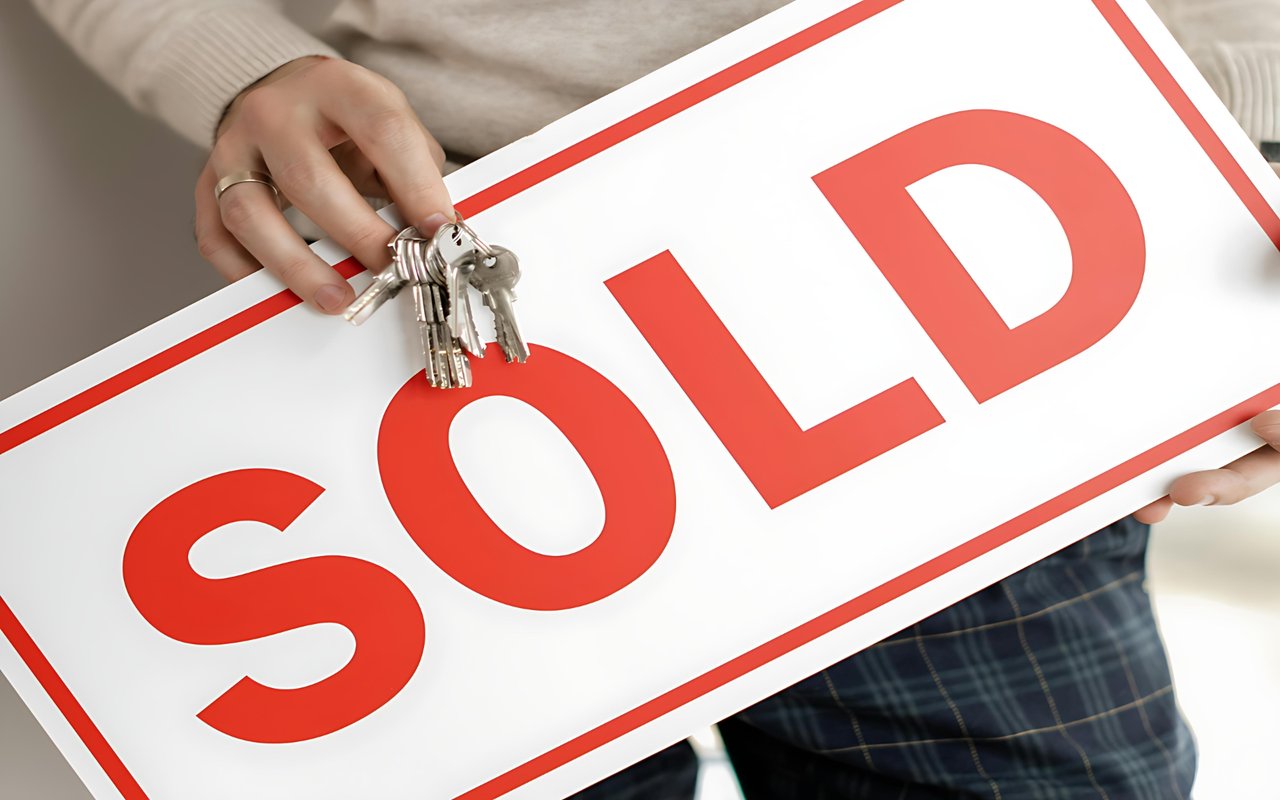A person holds a red-and-white SOLD sign with a set of keys.