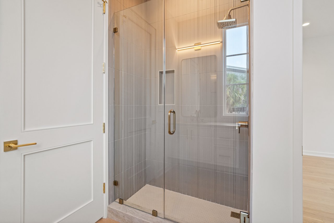 Walk-in shower with gray tile, brass fixtures, and a tall window.
