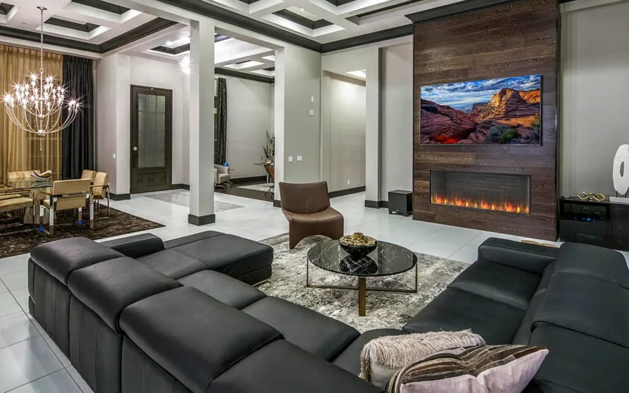 Modern living room with a dark sectional, glass coffee table, and wood-paneled fireplace wall.