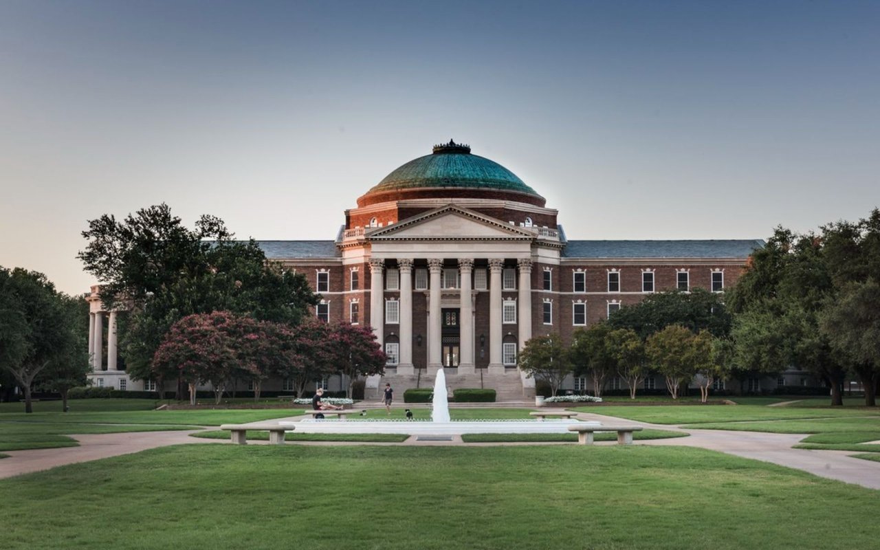 The grand limestone building and bell tower of Dallas Hall in the middle of the Southern Methodist University campus.