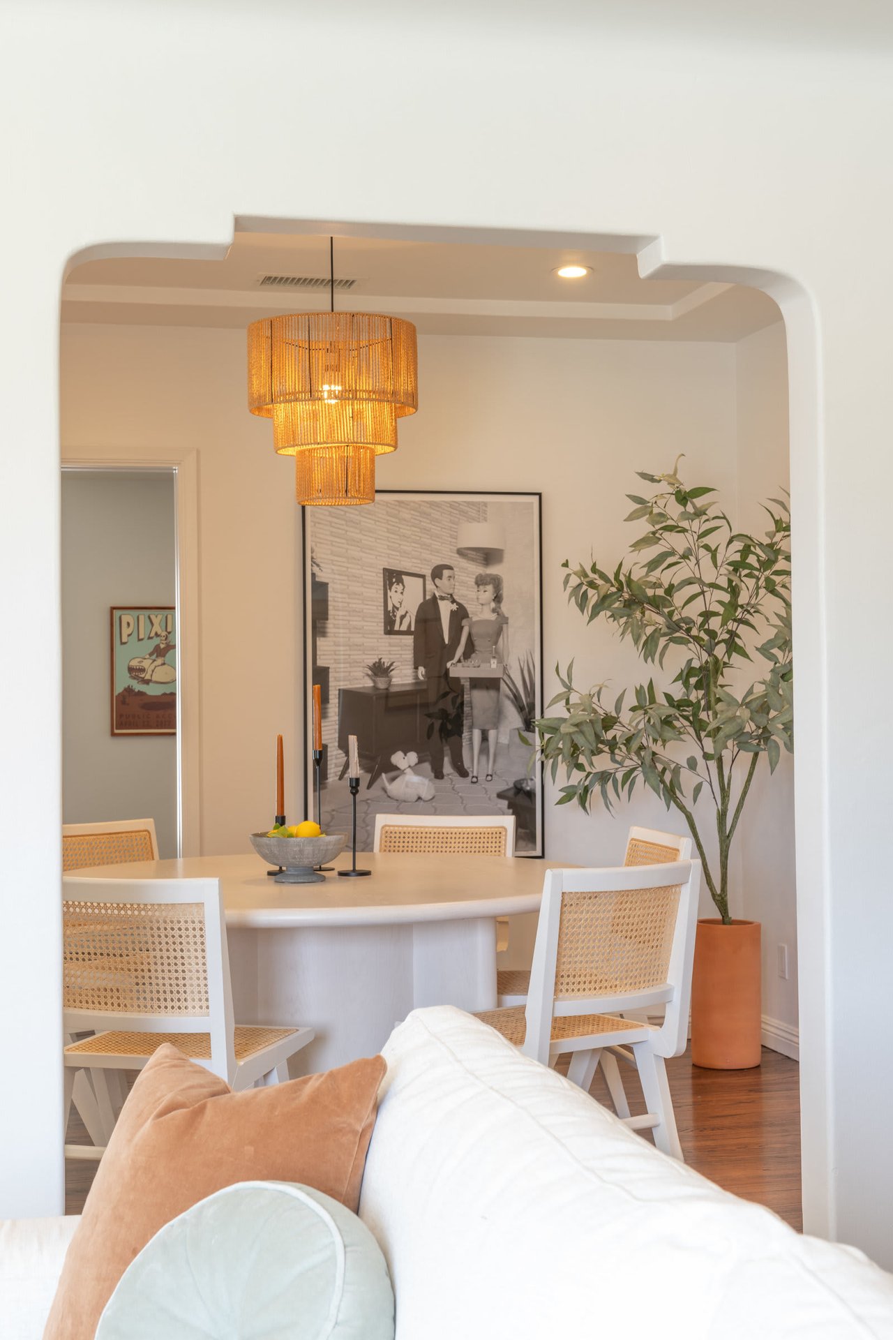 Cozy dining nook with round table, woven chairs, large black-and-white artwork, and rattan pendant light.