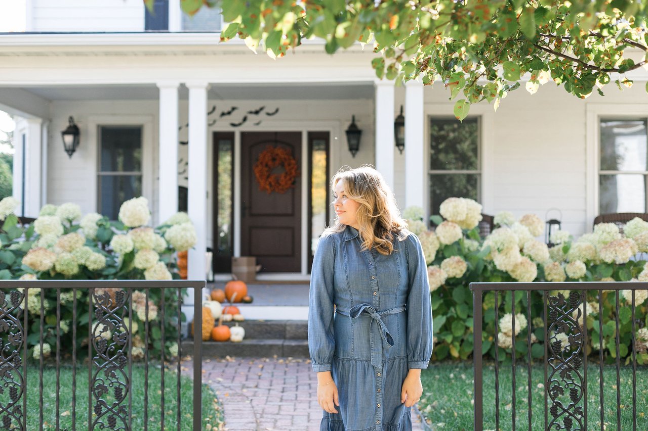 Woman standing outside a home decorated for Halloween with pumpkins, an orange wreath, and bats above the front door.
