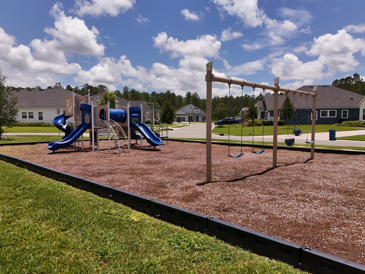 Neighborhood playground with blue slides and swings beside homes.