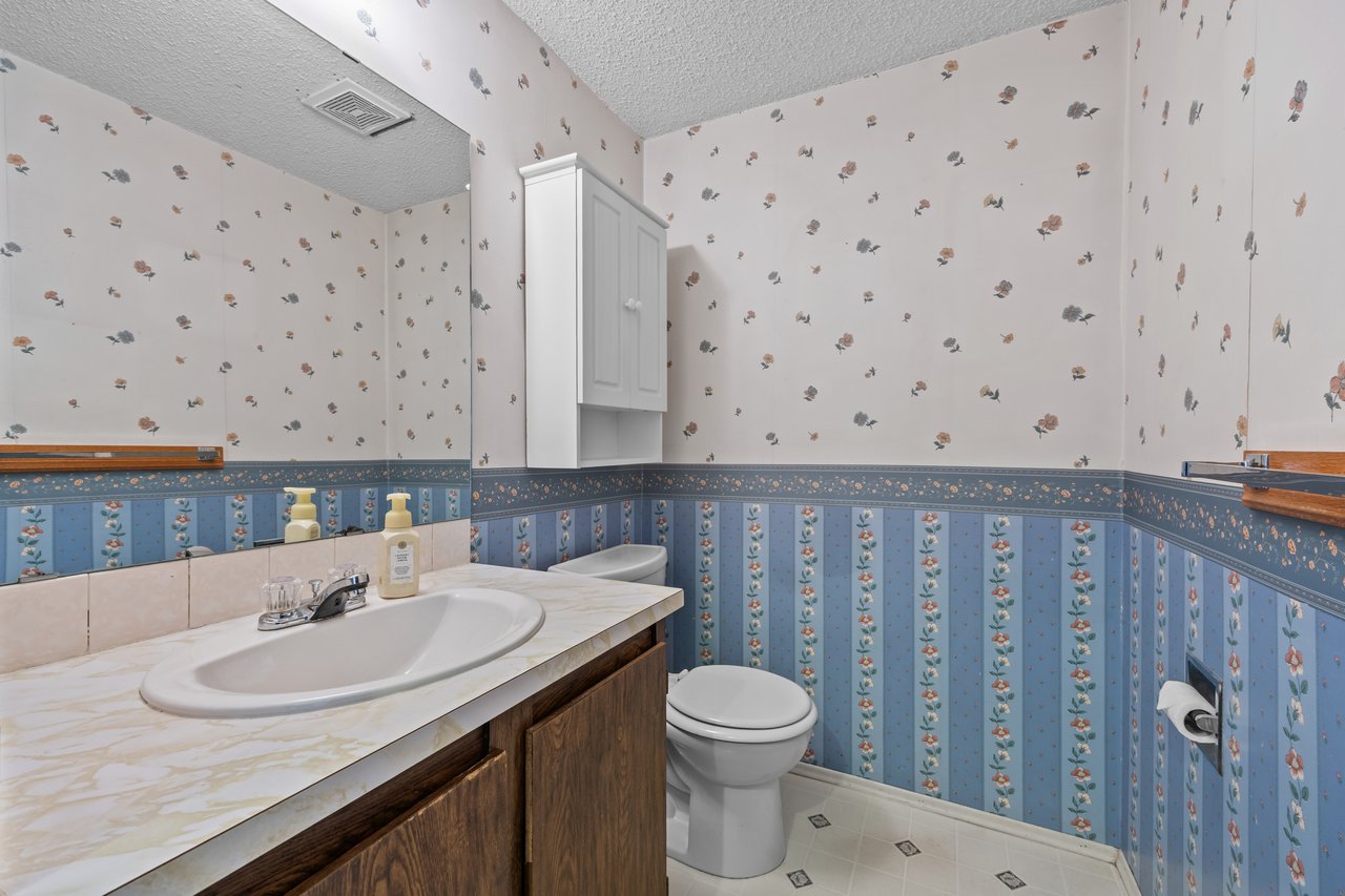 Bathroom with a marble-look vanity, toilet, and pink-and-blue floral wallpaper.