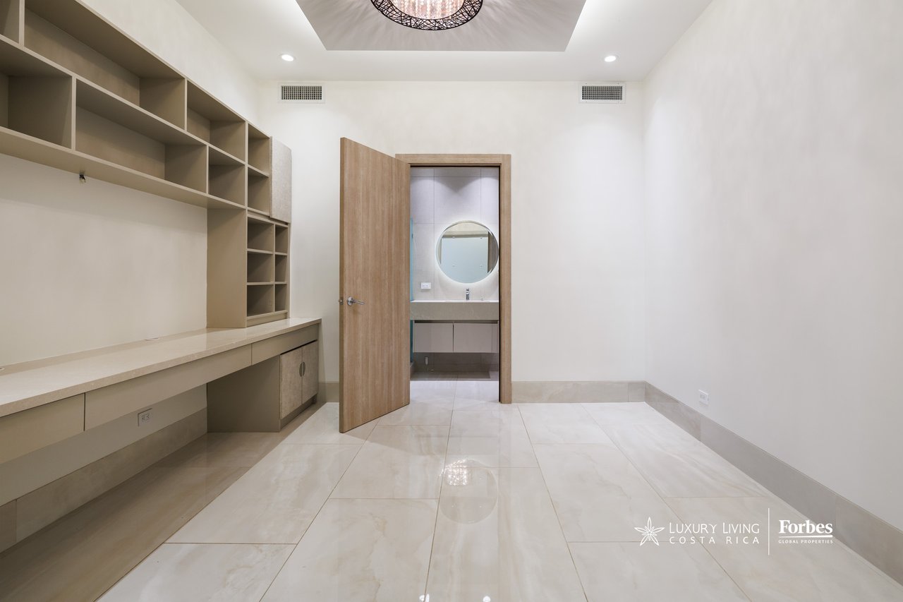 Built-in shelving and desk in a bright room opening to a bathroom with a round mirror.
