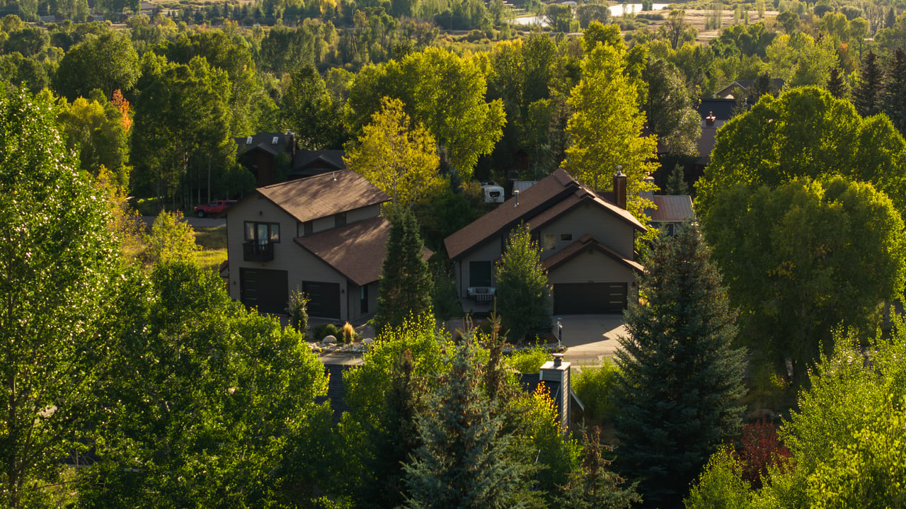 Two homes nestled among autumn trees, viewed from above in warm evening light.