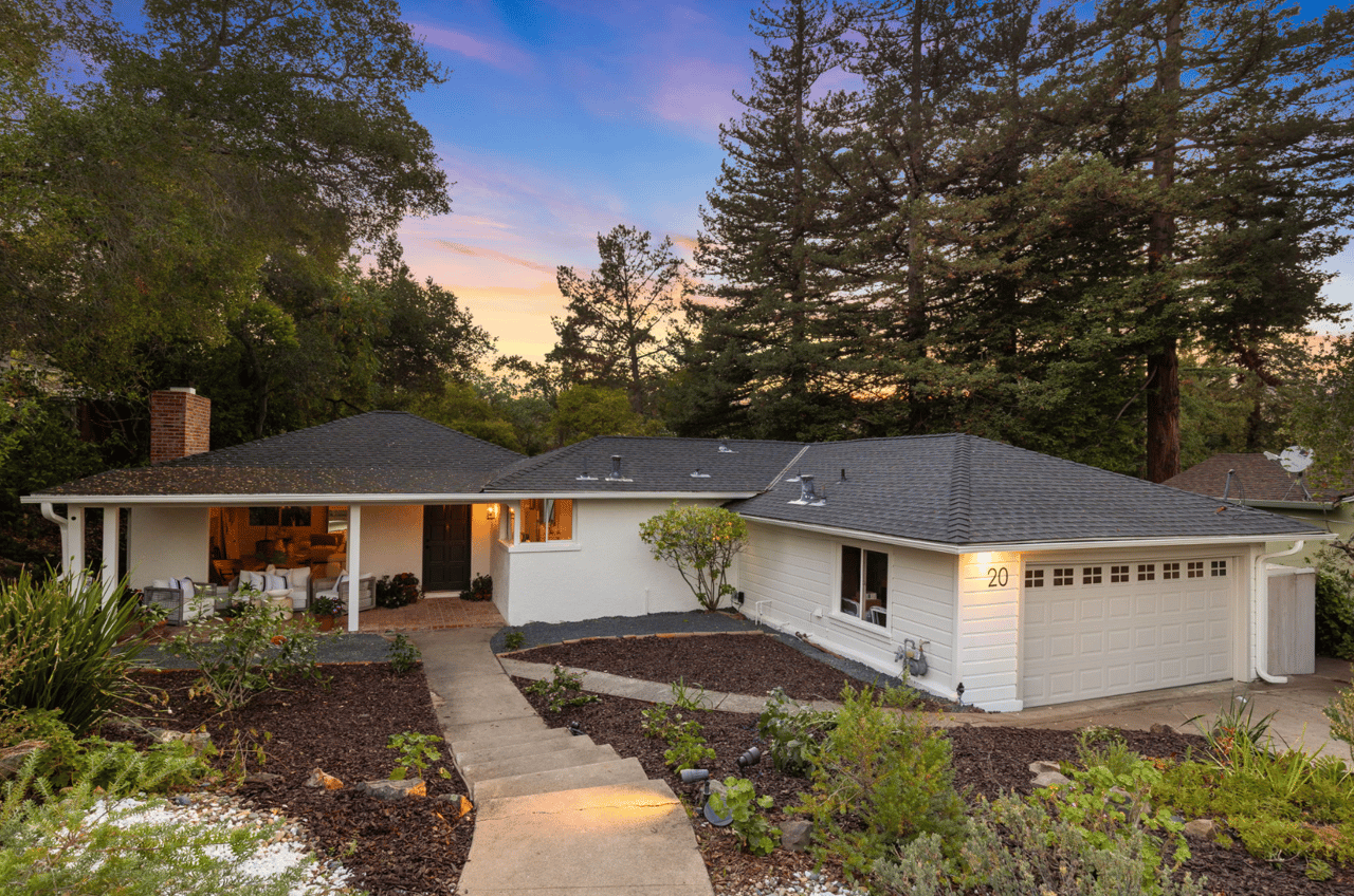 Single-story white house with an attached garage, covered patio, and landscaped walkway at dusk.