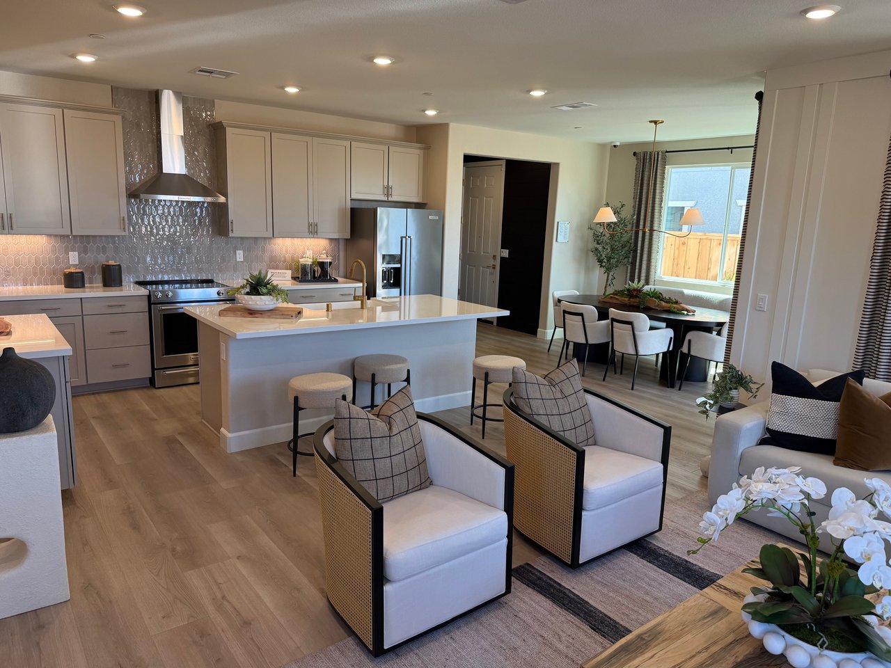 Open-plan kitchen with a large white island, stainless steel appliances, and a furnished dining and living area.