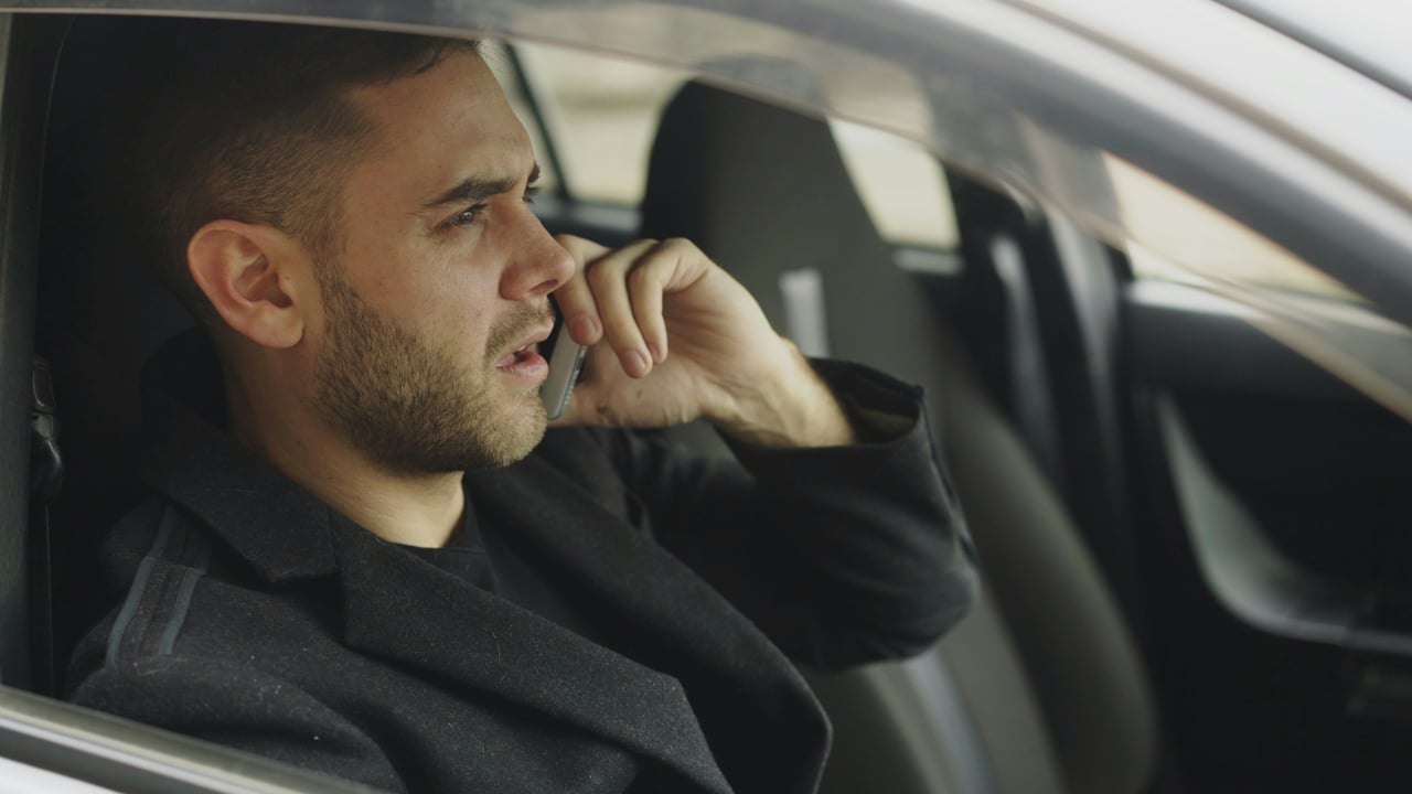 A man sitting in a car talking on his phone with a focused, contemplative expression