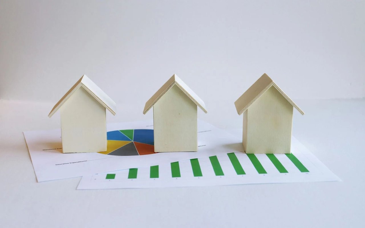 Three wooden house models stand on printed charts with rising green bars.