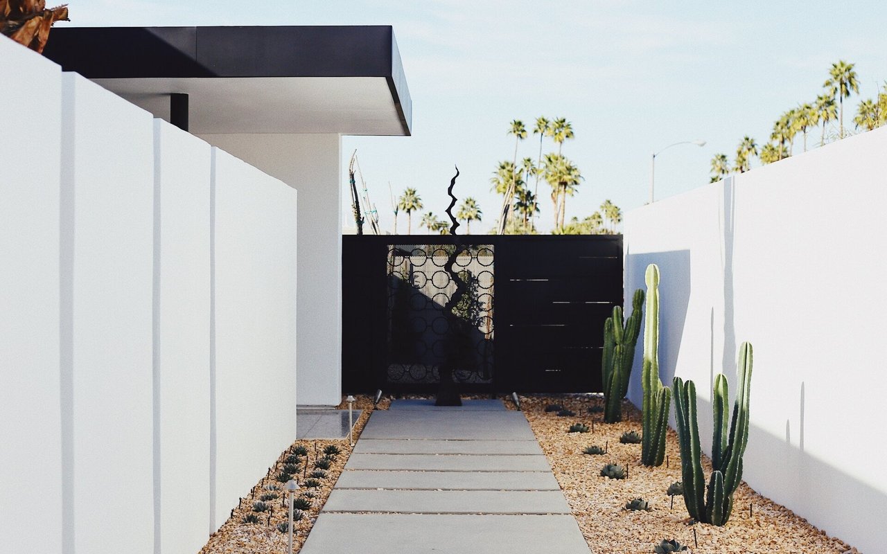 Modern home entrance with a concrete path, black gate, white walls, and desert landscaping.