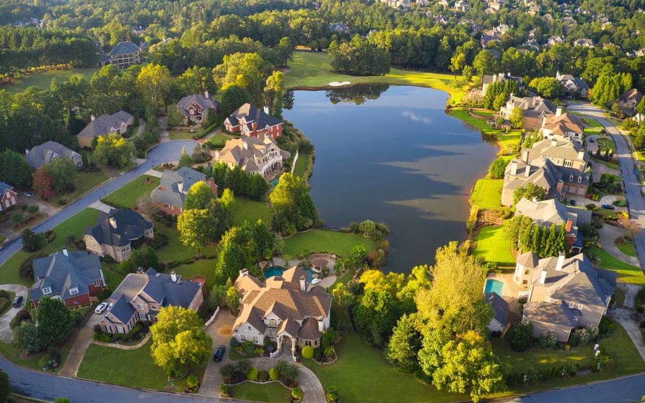 Aerial view of homes around a lake, with mature trees and manicured lawns.